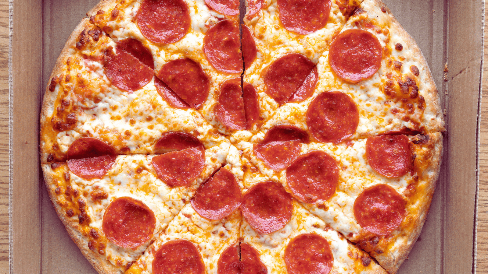 Pepperoni pizza cut into slices inside an open cardboard box, showing melted cheese and evenly spaced pepperoni on a golden crust.